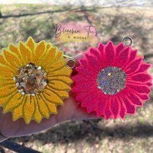 May include: Two resin sunflower keychains with glitter accents. One keychain is yellow and the other is pink.