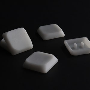 May include: Four white plastic keycaps for a mechanical keyboard. Three of the keycaps are blank, and one has two small raised bumps.
