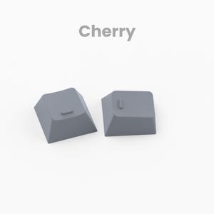 May include: Two gray plastic keyboard keycaps with the letters "L" and "J" printed on them. The keycaps are designed for Cherry MX mechanical keyboards.
