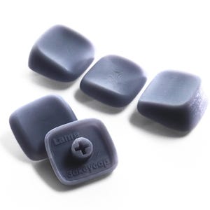 May include: A set of four matte grey square keycaps with rounded edges. One keycap is flipped over to reveal a cross-shaped stem mount on the underside, with the embossed text "Lame" and "3akeycap" visible on the base of the keycap surface.
