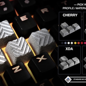 May include: Close-up of a mechanical keyboard with gray and black keycaps. The keycaps have a textured, chevron design. The image includes text that reads "PICK YOUR PROFILE / MATERIAL / FINISH".