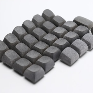 Könnte beinhalten: Nahaufnahme einer Anordnung dunkelgrauer, geometrisch geformter Schaumstoffstücke. Die Stücke haben eine strukturierte Oberfläche und abgerundete Kanten, vor einem weißen Hintergrund. Das Bild ist gut beleuchtet und hebt die Formen hervor.