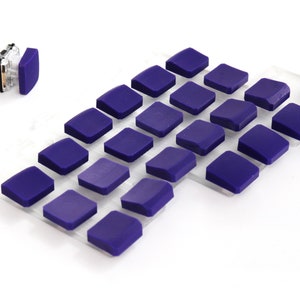 Könnte beinhalten: Eine Ansammlung kleiner, quadratischer, violetter Objekte, die auf einer transparenten, rechteckigen Oberfläche angeordnet sind. Ein Objekt ist abgelöst und zeigt eine transparente Kunststoffkomponente. Die Objekte sind gleichmäßig verteilt und leicht abgerundet.