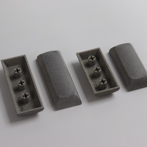 May include: Four gray plastic keycaps with a textured surface. Three of the keycaps have three small plus signs on the bottom. The fourth keycap is plain.