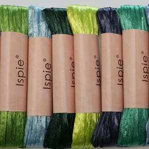 Peut inclure: Plusieurs bobines de ruban Isipie aux couleurs variées de bleu et de vert. Chaque bobine est enveloppée dans un papier brun clair avec le nom de la marque imprimé dessus. Les rubans ont un aspect texturé et froissé.