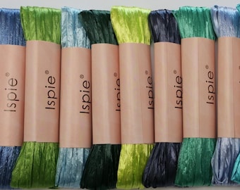May include: A selection of Isipie ribbon spools in various shades of blue and green. Each spool is wrapped in a light brown paper with the brand name printed on it. The ribbons have a textured, crinkled appearance.