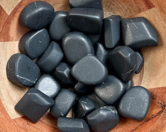 May include: A bowl filled with black tumbled stones. The stones are smooth and polished, with a variety of shapes and sizes.