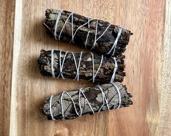 May include: Three bundles of dried sage, tied with white twine, on a wooden surface. The sage is brown and has a natural, earthy look.