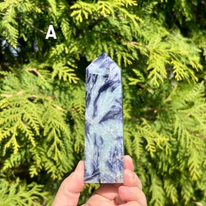 May include: A polished crystal tower labeled with the letter A, featuring a distinct pattern of deep purple and pale mint green mineral inclusions throughout the stone, shaped into a hexagonal point with a flat base and smooth, reflective surfaces.
