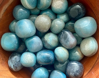 May include: A bowl filled with tumbled blue and gray agate stones. The stones are smooth and polished, with a variety of shades of blue and gray.