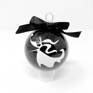 May include: Black and white Christmas ornament with a glittery black finish. The ornament features a white silhouette of Zero, the ghost dog from The Nightmare Before Christmas.