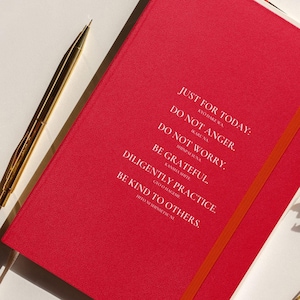 Peut inclure: Un journal rouge avec le texte "JUST FOR TODAY: DO NOT ANGER. DO NOT WORRY. BE GRATEFUL. DILIGENTLY PRACTICE. BE KIND TO OTHERS." Un stylo doré et des fleurs séchées sont à côté du journal.