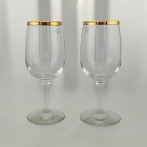 May include: Two clear glass wine glasses with a gold rim.