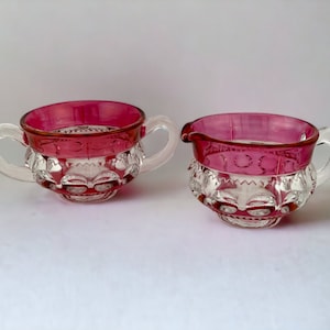 Puede incluir: Un juego de dos boles de azúcar y crema vintage de vidrio. Los boles son de vidrio transparente con un borde rojo cereza y diseños intrincados de vidrio cortado.