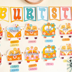 May include: A colourful classroom chart with a banner that reads "BURTSTA" and features a VW bus for each month of the year. Each bus has a flower design and the month's name in German. Below each bus are name tags with names written in different languages.