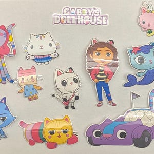 Könnte beinhalten: Eine Sammlung farbenfroher Gabby's Dollhouse-Aufkleber mit verschiedenen Katzencharakteren und Gabby selbst. Die Aufkleber umfassen ein lila Rennauto, eine Meerjungfrauenkatze und andere skurrile Designs. Der Text "GABBY'S DOLLHOUSE" ist oben abgebildet.
