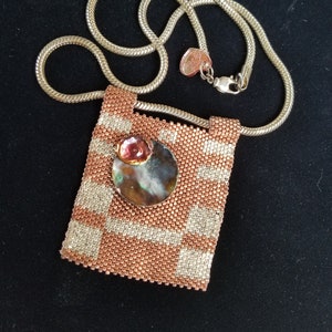 May include: A copper and white beaded necklace with a round, iridescent, copper-toned pendant. The pendant has a small pink accent.