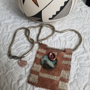 K&ouml;nnte beinhalten: Eine Halskette aus Kupfer- und Silberperlen mit einem Anh&auml;nger, der eine runde Abalone-Muschel mit einem rosa Blumenakzent zeigt. Die Halskette hat eine silberne Kette und einen kleinen Herzanh&auml;nger mit dem Text "Forever My Navy".