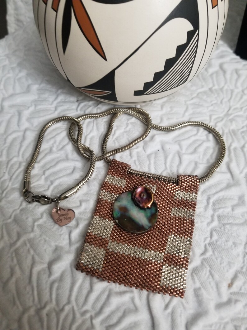 K&ouml;nnte beinhalten: Eine Halskette aus Kupfer- und Silberperlen mit einem Anh&auml;nger, der eine runde Abalone-Muschel mit einem rosa Blumenakzent zeigt. Die Halskette hat eine silberne Kette und einen kleinen Herzanh&auml;nger mit dem Text "Forever My Navy".