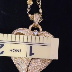 Puede incluir: Collar con colgante de coraz&oacute;n dorado con una cadena de cuentas. El colgante de coraz&oacute;n presenta un dise&ntilde;o texturizado en forma de pluma y una peque&ntilde;a gema transparente. El colgante mide aproximadamente 2,5 cm de ancho.