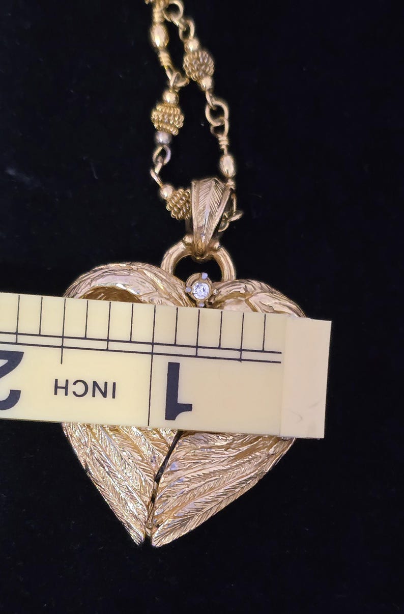 Puede incluir: Collar con colgante de coraz&oacute;n dorado con una cadena de cuentas. El colgante de coraz&oacute;n presenta un dise&ntilde;o texturizado en forma de pluma y una peque&ntilde;a gema transparente. El colgante mide aproximadamente 2,5 cm de ancho.