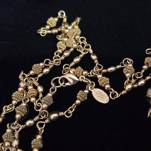 Puede incluir: Collar dorado con m&uacute;ltiples hilos y detalles intrincados. El collar presenta varias formas de cuentas, incluyendo peque&ntilde;as cuentas redondas y cuentas texturizadas y agrupadas. Se ve un cierre de langosta y una peque&ntilde;a etiqueta.
