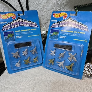 May include: Two Hot Wheels Micro Air Defenders color change spy plane sets in blue blister packaging. Each pack contains five miniature toy aircraft in various shades of gray, white, and olive green, along with black plastic flight sticks.