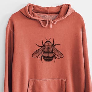 May include: A terracotta colored hoodie with a black and white illustration of a bumblebee on the front.