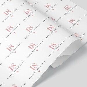 May include: White wrapping paper with a repeating pattern of the number 18 in a dusty rose color, along with the text "Happy Birthday Emily" and small hearts. The paper is partially rolled.