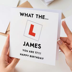 May include: A white birthday card with the text "WHAT THE... JAMES YOU ARE 17!!! HAPPY BIRTHDAY". The card features a red "L" in a gray square, a symbol for learner drivers.