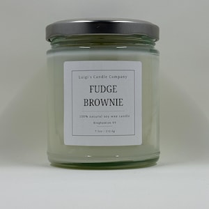 May include: A glass jar candle with a silver lid. The label reads "Luigi's Candle Company", "FUDGE BROWNIE", "100% natural soy wax candle", "Binghamton NY", and "7.5oz/212.6g".