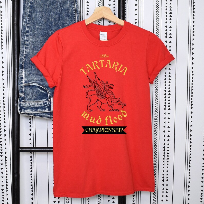 K&ouml;nnte beinhalten: Rotes T-Shirt mit einer schwarz-wei&szlig;en Grafik einer gefl&uuml;gelten Kreatur. Die Grafik enth&auml;lt den Text "1834 Tartaria mud flood championship".