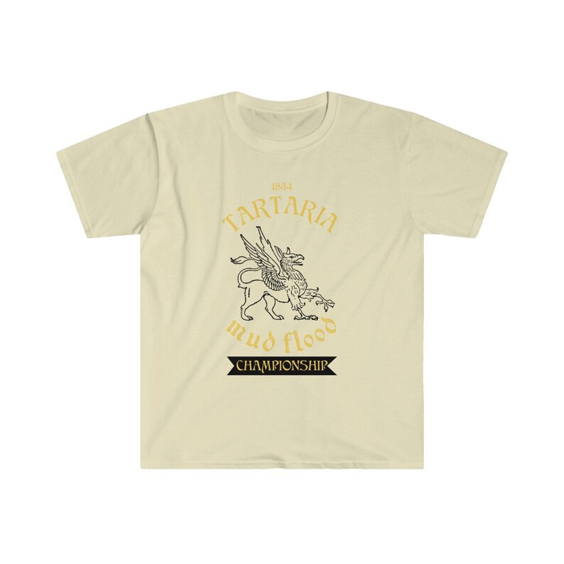 K&ouml;nnte beinhalten: Ein beiges T-Shirt mit einem schwarzen und goldenen Grafikdesign. Die Grafik zeigt einen gefl&uuml;gelten L&ouml;wen mit dem Text "1834 Tartaria mud flood championship".