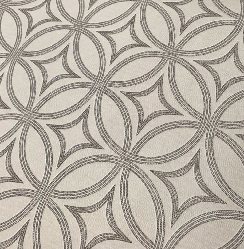 Op de afbeelding: Een witte stof met een herhalend patroon van overlappende cirkels en ruitvormige figuren in donkergrijs.