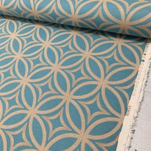 Op de afbeelding: Teal stof met een herhalend patroon van overlappende beige cirkels. De stof heeft een geweven textuur en is op zichzelf gevouwen. De rand van de stof is zichtbaar en heeft een witte rand met het nummer "032369" erop gedrukt.