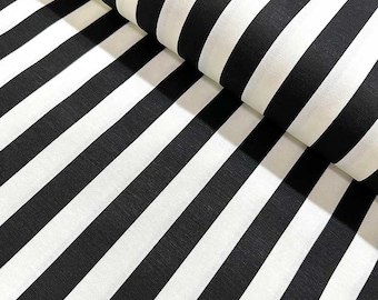 May include: Close-up of a fabric with bold, black and white stripes. The stripes run diagonally across the frame, creating a dynamic pattern. The fabric is folded over in the upper right corner, revealing the texture and depth of the material.