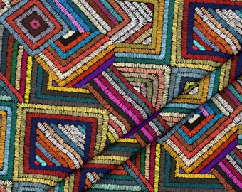 May include: A colorful fabric with a geometric pattern of overlapping squares. The fabric is made of a variety of colors, including red, orange, yellow, green, blue, purple, and black. The squares are outlined in black and have a textured appearance.