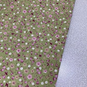 May include: Green fabric with a small pink and white floral print. The fabric is shown folded in half, with the printed side facing up.