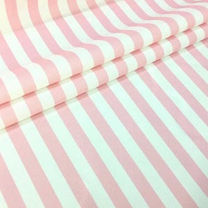 Op de afbeelding: Roze en witte gestreepte stof. De stof is gevouwen en toont het patroon van verticale strepen. De strepen wisselen af tussen zachtroze en wit, wat een klassiek ontwerp creëert. De stof lijkt van katoen of een vergelijkbaar materiaal te zijn.