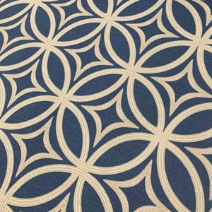 Op de afbeelding: Een close-up van een stof met een herhalend geometrisch patroon. Het patroon bestaat uit overlappende cirkels en ruiten in beige kleur op een donkerblauwe achtergrond.