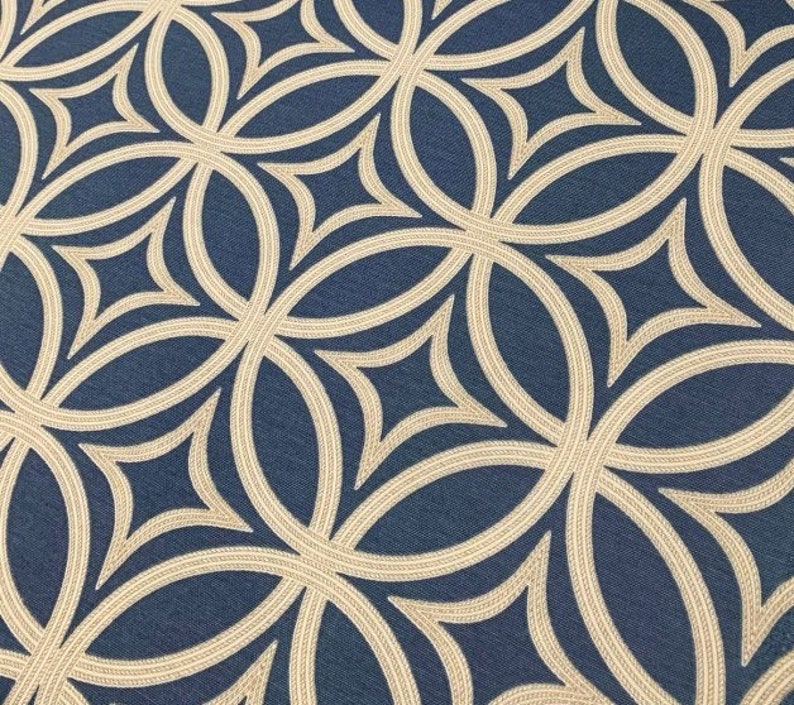 Op de afbeelding: Een close-up van een stof met een herhalend geometrisch patroon. Het patroon bestaat uit overlappende cirkels en ruiten in beige kleur op een donkerblauwe achtergrond.