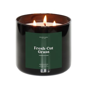 May include: A black glass candle jar with a green label that reads "Fresh-Cut Grass" and "Premium Wax Blend". The label also includes the text "MALADAK Candles Est. 2023" and "MINT COLLECTION | Jar Candle | Hand-poured | Made with essential oils".