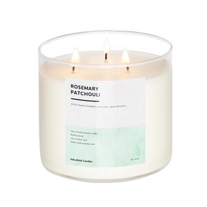 Puede incluir: Una vela de vidrio transparente con tres mechas. La vela es blanca y tiene una etiqueta que dice "Rosemary Patchouli" con las notas "Romero español, hoja de clavo, limón, pachulí". La etiqueta también dice "13oz 3-wick scented candle, hand-poured, soy-coconut wax, made with essential oils" y "NALADAK Candles, Est. 2023".