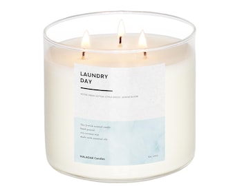 Peut inclure: Une bougie en verre transparent avec trois mèches. La bougie est étiquetée "Laundry Day" avec les notes "Fresh Cotton, Citrus Breeze, Jasmine Bloom". La bougie est coulée à la main avec de la cire de soja et de noix de coco et des huiles essentielles. L'étiquette indique également "Naladak Candles" et "Est. 2023".