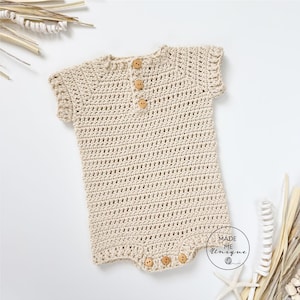 Può includere: Un pagliaccetto all'uncinetto beige con maniche corte e bottoni in legno. L'indumento per bambini fatto a mano presenta un motivo a punto strutturato ed è progettato con uno scollo tondo. Il pagliaccetto ha bottoni sul fondo per facilitare il cambio del pannolino.