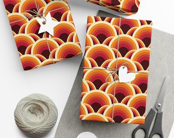 Può includere: Tre scatole regalo avvolte in carta da regalo retrò arancione, rossa e marrone. La carta presenta un motivo ripetitivo di cerchi concentrici. Le scatole sono legate con spago e decorate con etichette di carta bianca.