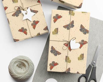 Puede incluir: Tres cajas de regalo envueltas en papel beige con un patrón de mariposas rojas y marrones. Las cajas están atadas con hilo y decoradas con etiquetas de papel blanco.