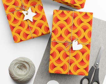Può includere: Tre scatole regalo avvolte in carta da regalo con motivo geometrico arancione e giallo. La carta presenta un motivo ripetitivo di cerchi concentrici. Le scatole sono legate con spago e decorate con stelle e cuori di carta bianca.