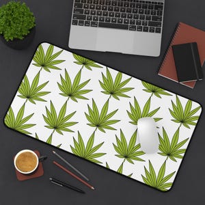 May include: A white desk mat with a green leaf pattern. The mat is designed to be used with a computer mouse and keyboard.