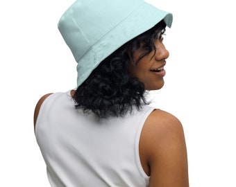 May include: A woman wearing a light blue bucket hat with a white tank top.